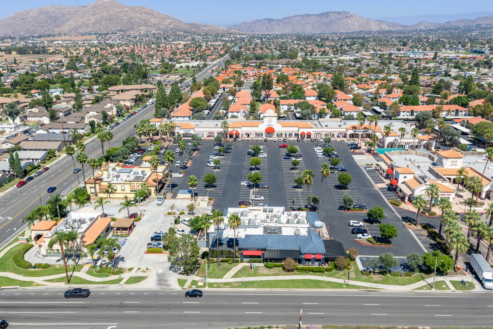 Aerial view of the full Plaza Del Sol site with the inline shops, both restaurant pads, the parking lot, and the mountains behind