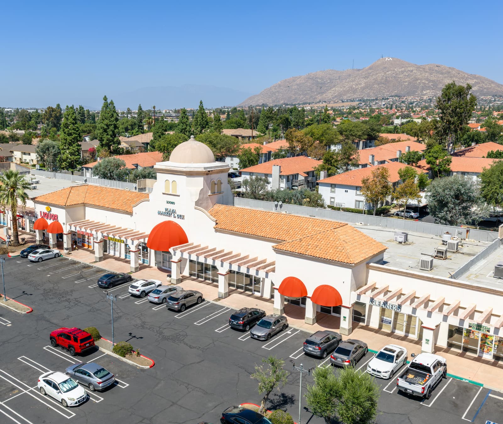 Plaza Del Sol's storefront row from above the parking lot: the domed tower entrance, red awnings, and the mountains behind