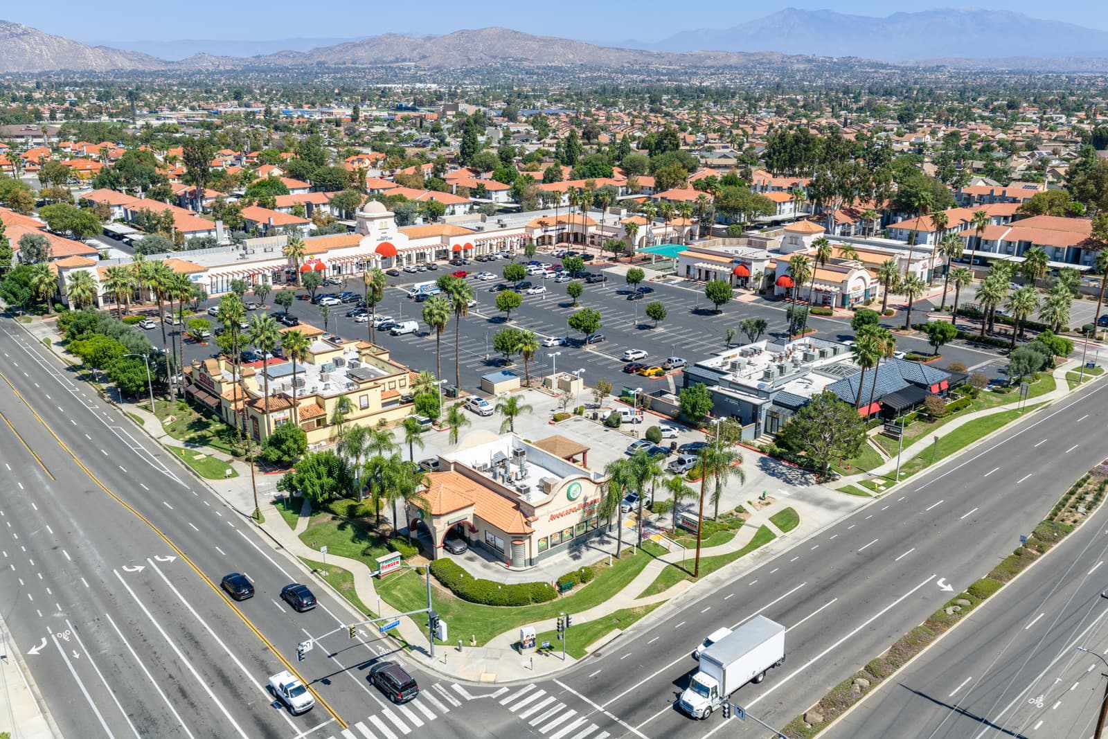 Avocado Burger drive-thru pad at the Alessandro Boulevard and Frederick Street corner of Plaza Del Sol, with the full center and mountains behind
